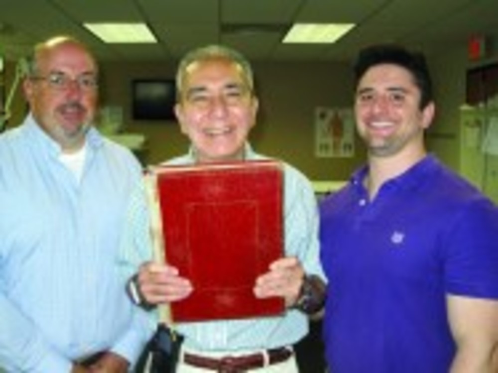 John McLinden, left, and Marc Bochner, right, physical therapists with Liberty Physical Center, stand at the Center with longtime client, Father Joe Haggar, who is holding a heavy book as part of his physical rehabilitation.
